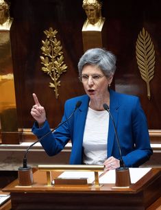 a woman giving a speech in front of a podium with her hand up to the side