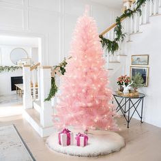 a pink christmas tree with presents on the floor next to it and stairs in the background