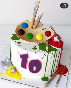 a birthday cake decorated with an artist's palette and paintbrushes on top