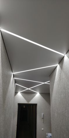 an empty hallway with white walls and lights on the ceiling, in front of a doorway