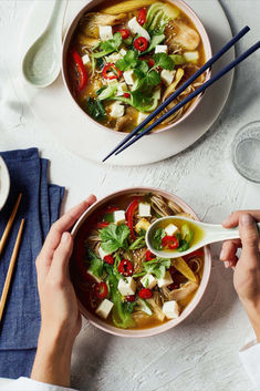 two bowls of soup with chopsticks on the side and one bowl filled with vegetables