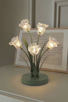 a vase with flowers on top of a table next to a framed photograph and paper