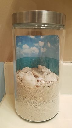 a glass jar filled with sand and water on top of a white counter next to a wall