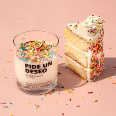 a piece of cake next to a candle on a pink surface with sprinkles