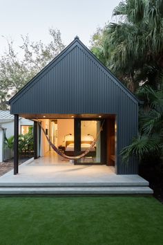 a house with a hammock hanging from it's roof and grass in the front yard