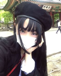 a woman with long black hair wearing a hat and holding her nose to her mouth