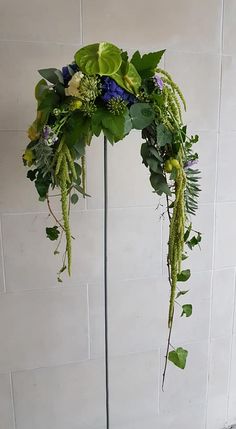 an arrangement of flowers and greenery is arranged on a metal pole in front of a white brick wall