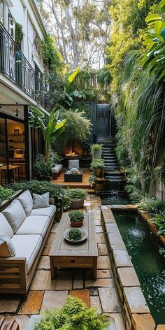 an outdoor living area with couches, tables and water feature in the center surrounded by greenery