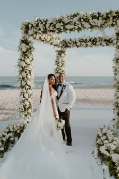 a bride and groom pose for a photo in front of an archway decorated with flowers