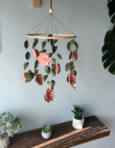 a mobile with flowers hanging from it's sides on a shelf next to a potted plant