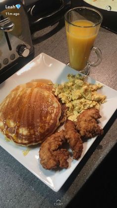 a white plate topped with pancakes and fried chicken next to a glass of orange juice