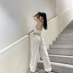 a woman standing on some stairs with her hand in her hair and wearing white pants