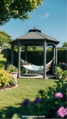 Garden gazebo with a hammock, surrounded by colorful flowers and greenery under a clear blue sky. Cozy Gazebo