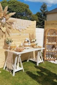 a table with cakes and desserts on it in front of a wooden sign that says,