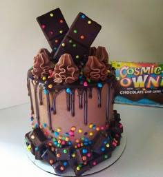 a chocolate cake with candy and candies on the top is next to a box of cosmic own