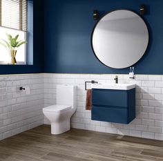 a white toilet sitting next to a blue sink in a bathroom under a round mirror