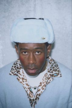 a man wearing a white hat and leopard print scarf with his eyes wide open in front of the camera