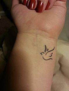 a woman's wrist with a small bird tattoo on the left side of her arm