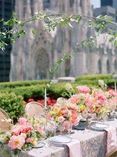 a long table is set with flowers and candles for an outdoor wedding reception in front of a cathedral