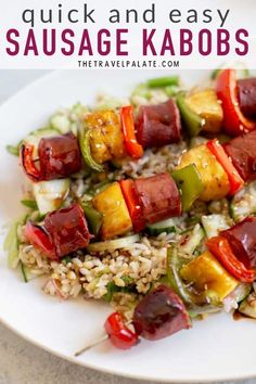 a white plate topped with meat and veggies on skewers next to rice