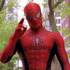 a man in a spider suit is making the v sign with his hand while standing outside