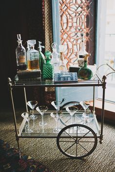 a bar cart with liquor bottles and glasses on it sitting in front of a window