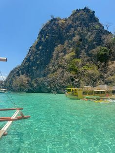 the water is crystal blue and clear, with boats in front of a large mountain