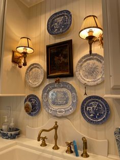 blue and white plates hang on the wall above a sink in a room with two lamps