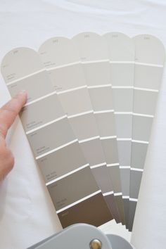 a hand is pointing at some gray paint swatches