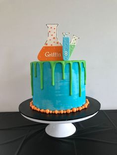 a birthday cake with blue icing and green drips on the top is sitting on a black table