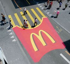 an aerial view of people walking on the sidewalk near a mcdonald's sign painted on the street