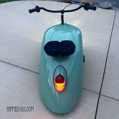 a green scooter with a black seat and tail light on the sidewalk next to some rocks