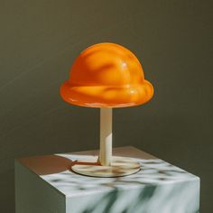 an orange lamp sitting on top of a white box next to a shadow covered wall