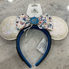 a mickey mouse ears headband with a blue bow on it's side and a tag attached to the ear