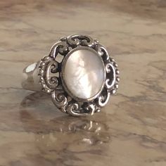 This sterling silver ring feels good and solid and heavy on your finger. It has a 10mm x 12mm oval faux mother of pearl/moonstone cabochon that almost has a cats-eye look, with a pretty pearliness to it. It is surrounded by elaborate scrollwork and flat beading on the shoulders. It is size 6.5 and comes in a colorful presentation box. Adjustable Elegant Moonstone Ring Oval Cabochon, Silver Oval Mother Of Pearl Rings, Silver Oval Rings With Mother Of Pearl, Elegant Oval Cabochon Moonstone Ring Stamped 925, Vintage Silver Oval Pearl Ring, Elegant Oval Nickel-free Moonstone Ring, Elegant Oval Moonstone Nickel-free Ring, Adjustable Silver Moonstone Ring In Oval Cabochon, Adjustable Silver Moonstone Ring With Oval Cabochon