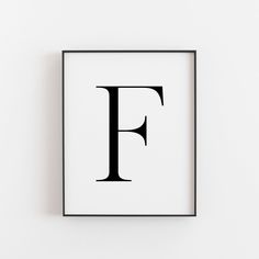 the letter f is displayed in a black frame on a white wall, with an empty space underneath it