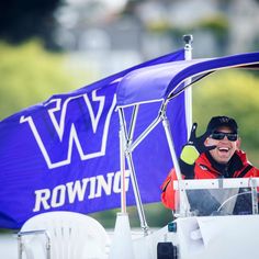 a man sitting in the cockpit of a small boat with a blue flag behind him