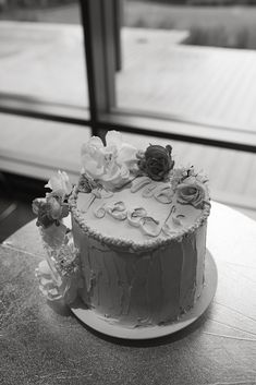 a white cake with flowers on it sitting on a table next to a large window