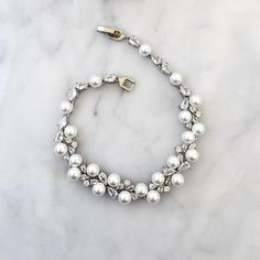 Classy and elegant, this delicate bracelet will add a touch of sophistication to any wedding gown or formal ensemble. It is featuring iridescent pearls and intricately faceted clear cubic zirconia that capture the light from every angle, sparkling beautifully. The bracelets are gold / rhodium plated for a flawless finish which perfectly enhances the intricate detailing and conveys a modern take on old elegance. Length: 7.5" (approx. 19cm); Width: and 0.4" (approx. 1cm); Weight: 7.3g. Closure is Formal Pearl Embellished Bracelet Jewelry, Formal Pearl Embellished Bracelet, Elegant Crystal Embellished Jewelry With Cubic Zirconia, Elegant Pearl Drop Bracelet For Party, Elegant Pearl Chain Beaded Bracelet For Formal Occasions, Elegant Pearl Bracelets For Party, Elegant Pearl Bracelet For Party, Formal White Pearl Embellished Bracelets, Formal White Pearl Bracelets