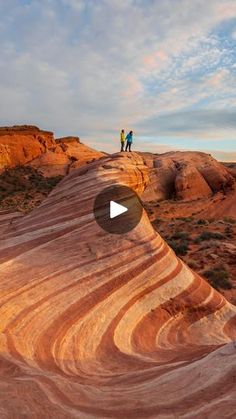 two people standing on top of a large rock formation in the middle of an arid area