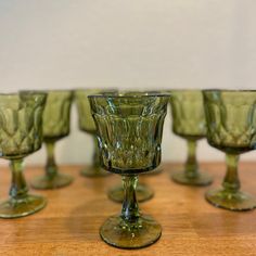 four green glass goblets sitting on top of a wooden table next to each other