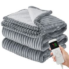 a person holding an alarm clock next to a stack of blankets with thermometer in their hand