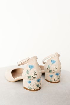 a pair of white shoes with blue flowers painted on the upper part of each shoe