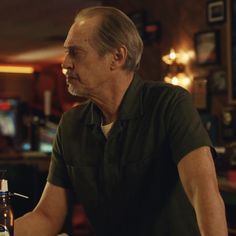 an older man sitting at a table with a bottle of beer in front of him