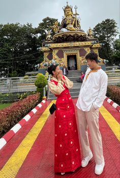 a man standing next to a woman in a red and yellow dress near a statue