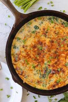 an omelet in a cast iron skillet with green onions on the side