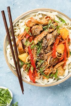 a bowl filled with noodles, meat and veggies next to chopsticks