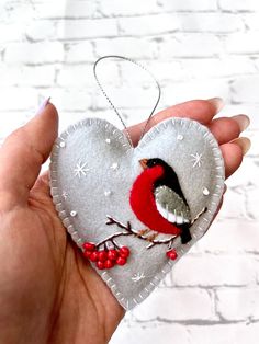 a hand holding a heart shaped ornament with a bird on it