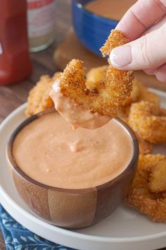 a person dipping some food into a small bowl on a plate with other foods in the background