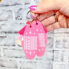 a person holding two pink and white keychains with words written on the front